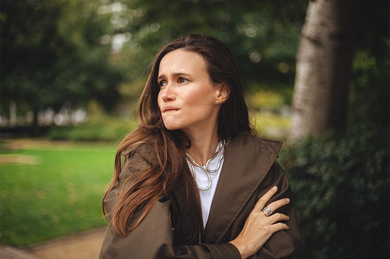 A woman sitting outdoors, looking away in thought.