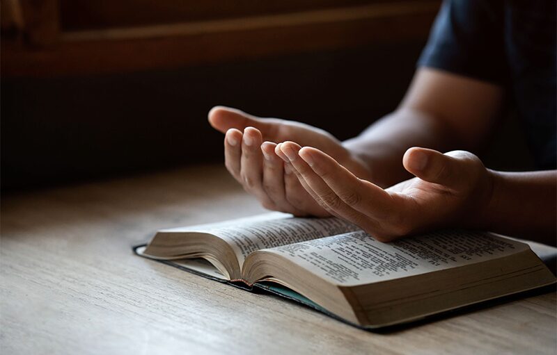 A pair of hands resting on an open Bible in low, warm light.