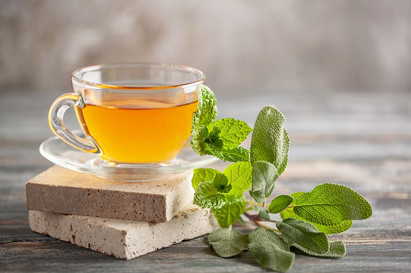 A cup of herbal tea with fresh mint on a stone slab.