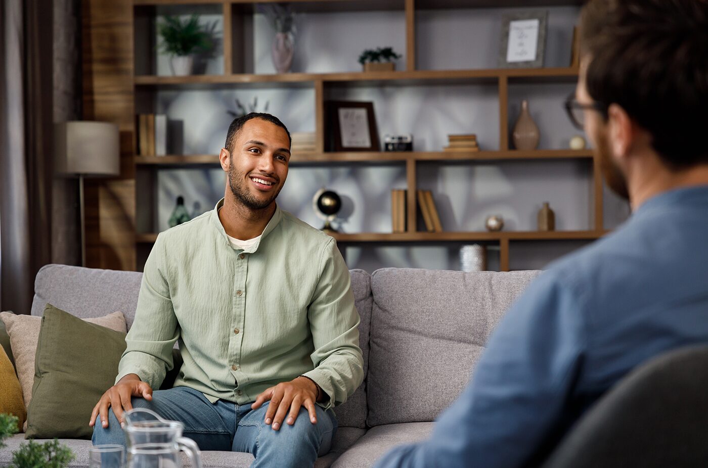 A man sitting forward on a couch mid-conversation, listened to closely by his therapist.