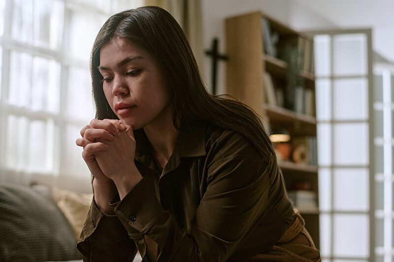 A woman with her head bowed and her hands clasped in prayer.