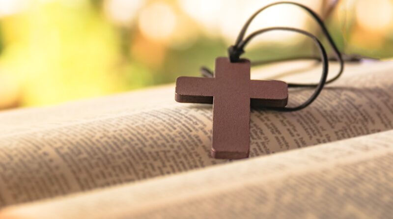 A small wooden cross on a leather cord resting on a worn armrest.